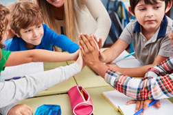 Kinder am Tisch geben sich "High five". Foto: Robert Kneschke - stock.adobe.com