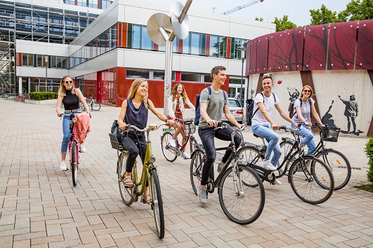 Studierende treffen sich mit ihren Fahrrädern vor dem Erweiterungsbau und Schloss