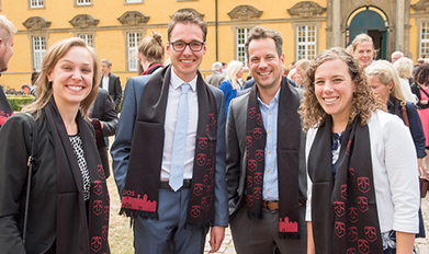 Four young people laugh into the camera, wearing festive scarves.